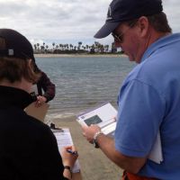 Two people on a shoreline looking at clipboards.