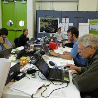 People at a crowded table with computers and maps.