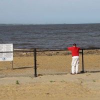 Person standing at a fenced-off beach closed to the public.