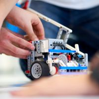 Student hands are seen constructing a machine out of Legos.