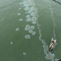 Aerial image of oil emerging in an area of containment boom. A response vessel is seen in the lower right of the image.