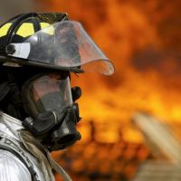 Man in chemical protective mask with fire in background.