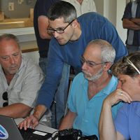 Four individuals direct their attention to a laptop computer screen.